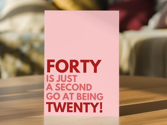 A pink 40th birthday card with bold red text reading 'FORTY IS JUST A SECOND GO AT BEING TWENTY!' 