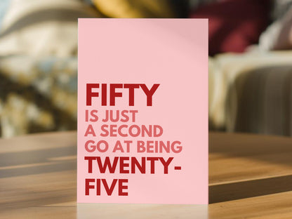 A pink 50th birthday card with bold red text reading 'FIFTY IS JUST A SECOND GO AT BEING TWENTY-FIVE'.