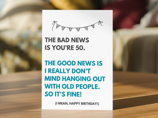 A 50th birthday card with a humorous quote that reads "THE BAD NEWS IS YOU'RE 50. THE GOOD NEWS IS I REALLY DON'T MIND HANGING OUT WITH OLD PEOPLE SO IT'S FINE! (I MEAN, HAPPY BIRTHDAY!)