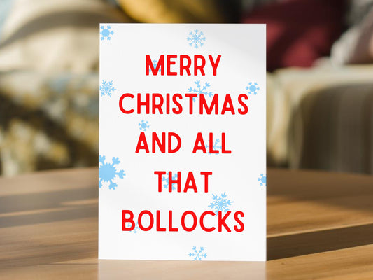 A funny Christmas card standing with red text reading 'MERRY CHRISTMAS AND ALL THAT BOLLOCS' and light blue snowflake accents