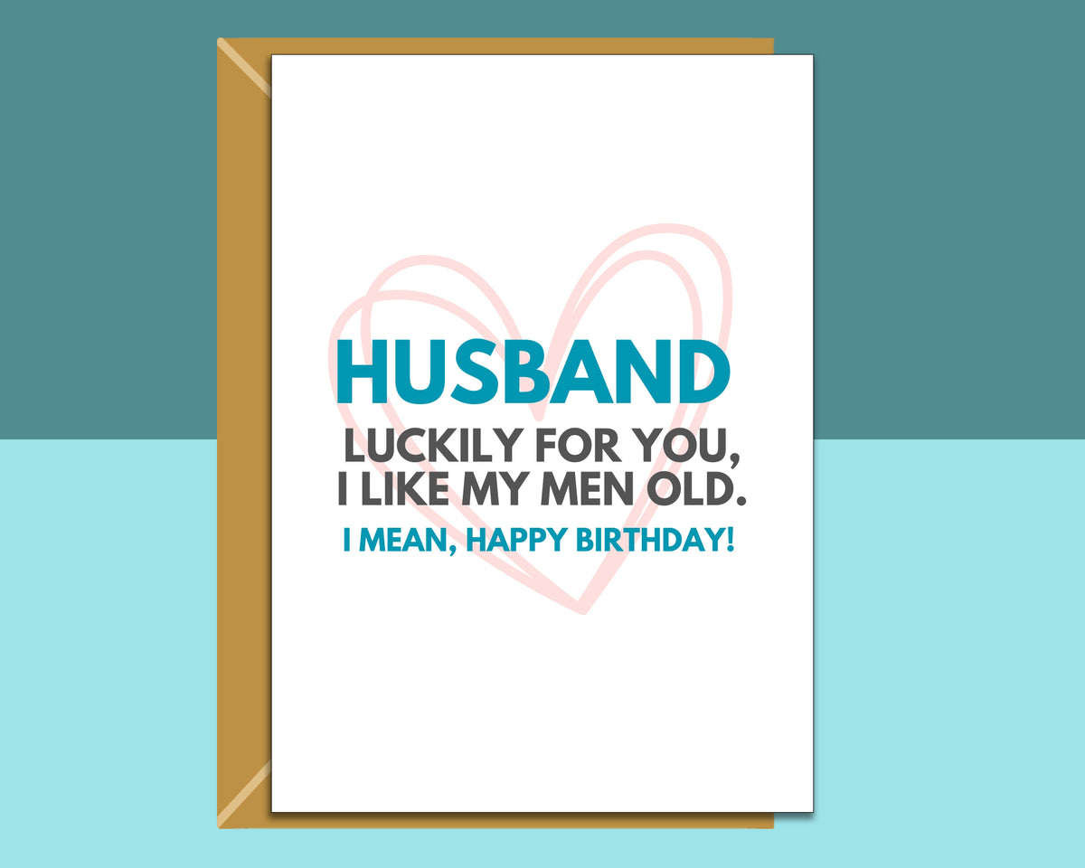 A birthday card for a husband with a kraft envelope, featuring a white card with blue and black text and a light pink heart outline, set against a split teal and light blue background.