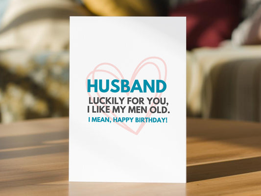 A white birthday card for a husband. The card reads, 'HUSBAND LUCKILY FOR YOU, I LIKE MY MEN OLD.