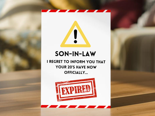 A funny son-in-law 30th birthday card. The card is white with a red and white hazard border, a yellow warning triangle, black text reading 'SON-IN-LAW I REGRET TO INFORM YOU THAT YOUR 20'S HAVE NOW OFFICIALLY.