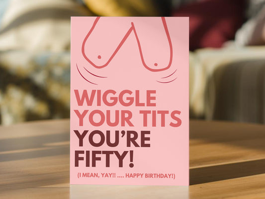 A pink funny 50th birthday card with a winking breasts graphic and the text 'WIGGLE YOUR TITS YOU'RE FIFTY! (I MEAN, YAY!! .