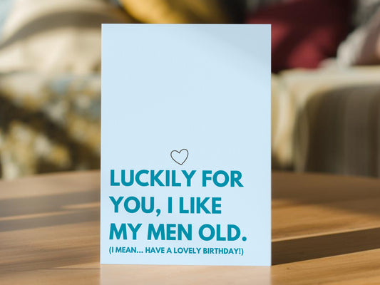 A light blue greeting card with a humorous birthday message reading "Luckily for you I like my men old (I mean... have a lovely birthday!) printed in darker blue. For boyfriend, husband, fiance.